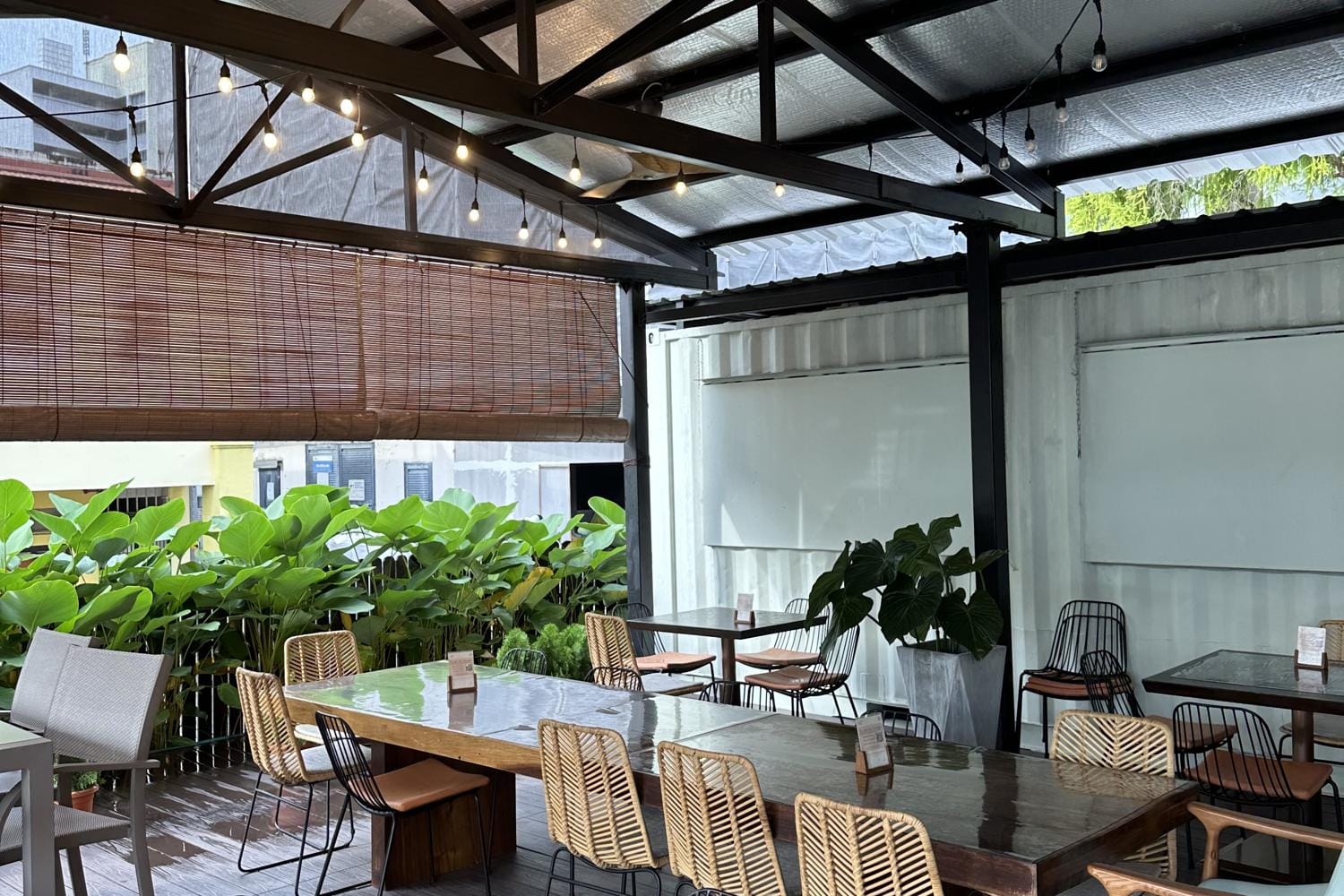 A covered rooftop terrace set with long dining tables under festoon lights
