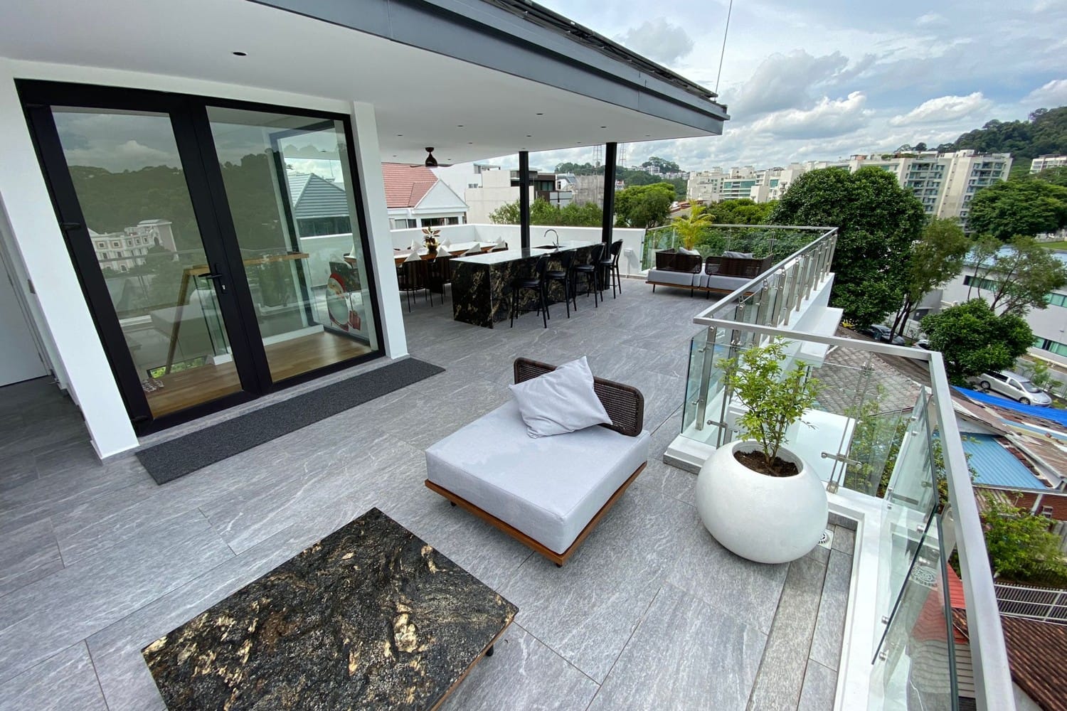 A rooftop terrace with a bar counter and day bed, looking over low-rise housing