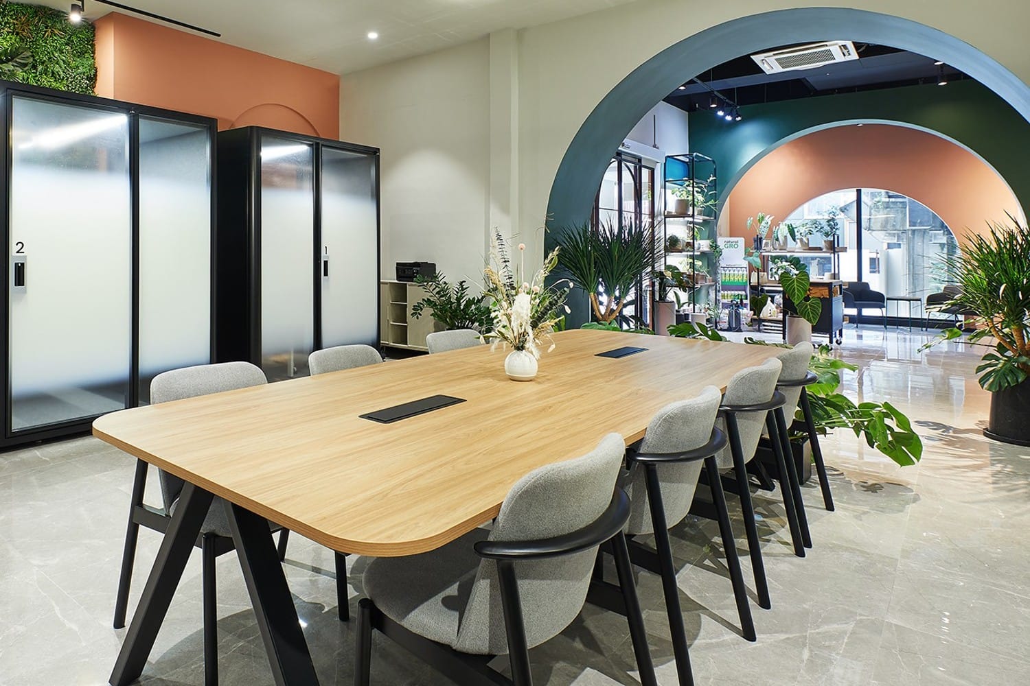 A long wooden meeting table with grey chairs in front of a teal archway.