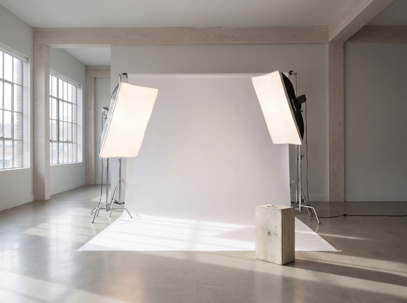 A photography studio with a white paper backdrop, two softboxes and a concrete floor